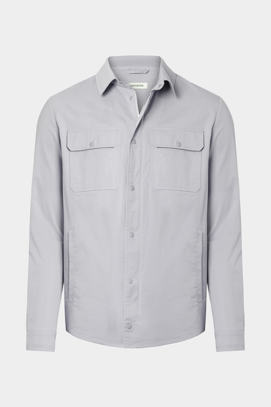 Vue sur fond blanc d'une surchemise en 100% coton gris clair avec fermeture zippée et pression boutonnée et poches à rabat boutonnés.