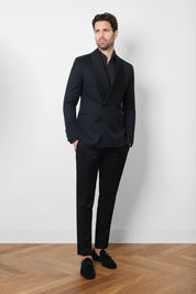Vue sur mannequin un smocking noir croisé avec un large revers col châle et un pantalon taille haute ceinture large en satin de soie et patte de serrage.