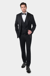 Un homme aux cheveux courts et foncés porte une chemise de smoking blanche avec un nœud papillon noir. Il porte également un costume coupe smoking trois pièces. Sa tenue est assortie à des mocassins noirs en cuire.
