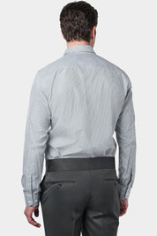Un homme de dos vêtu d'une chemise à rayures kaki et blanches avec un col français. Il porte également un pantalon gris foncé à pinces, accompagné de mocassins en daim marron.L'homme se tient debout, les mains détendues le long du corps, sur un fond gris clair uni.