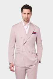 Un homme portant un costume croisé à revers pointus en rose poudré. Il a une pochette de costume rouge et bleue dans la poche de sa veste ainsi qu'une chemise rayée rose et blanche sous son costume.