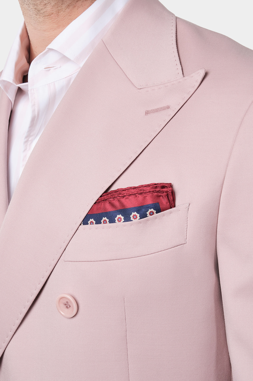 Vue rapprochée des revers pointues du costume rose poudré et de la pochette de costume rouge et bleue présent dans la poche de la veste.