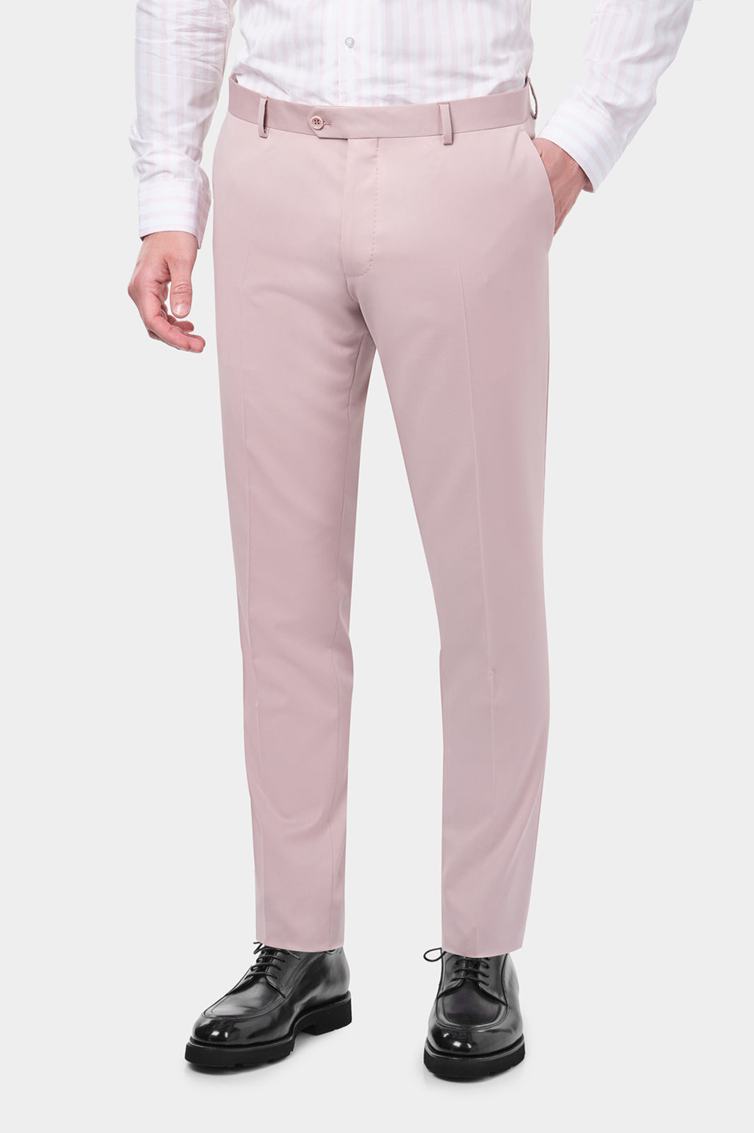 Plan rapproché du pantalon de costume rose poudré. L'homme porte également des souliers en cuir noir et une chemise rayée rose et blanche.