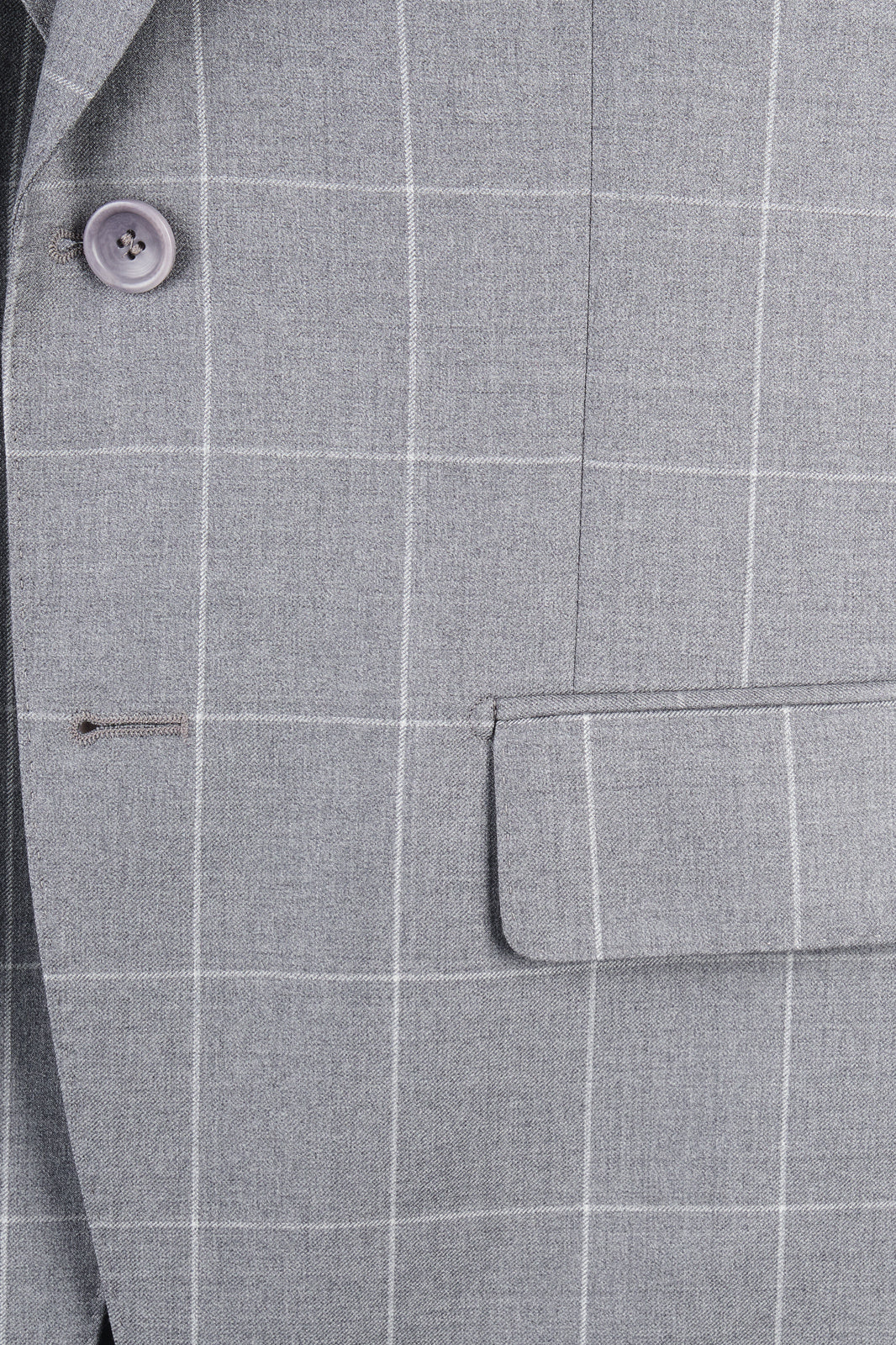Zoom sur la matière et la poche plaquée de la veste du costume gris à carreaux.