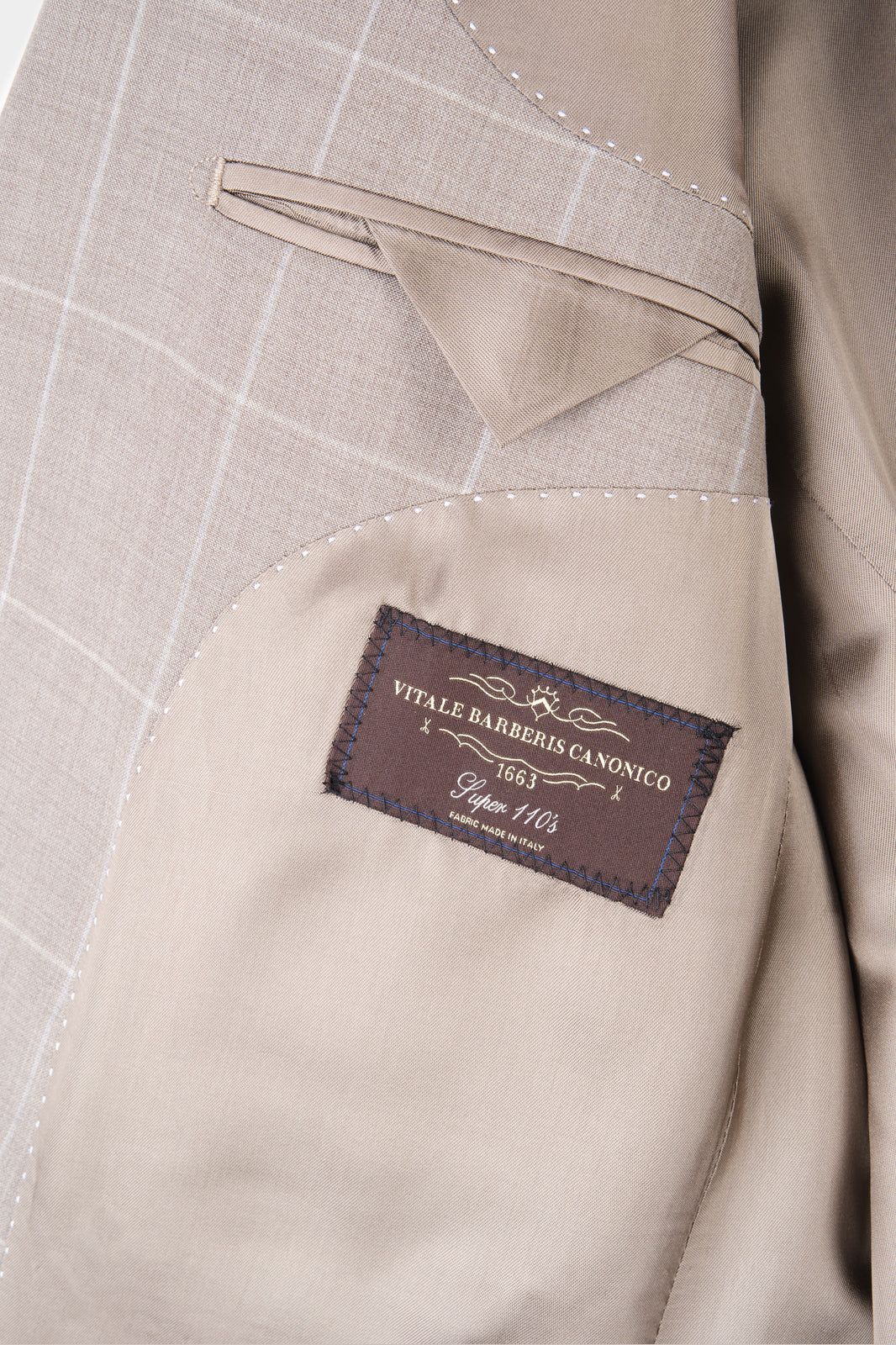 Zoom sur l’étiquette et la poche intérieure de la veste du costume beige à carreaux.
