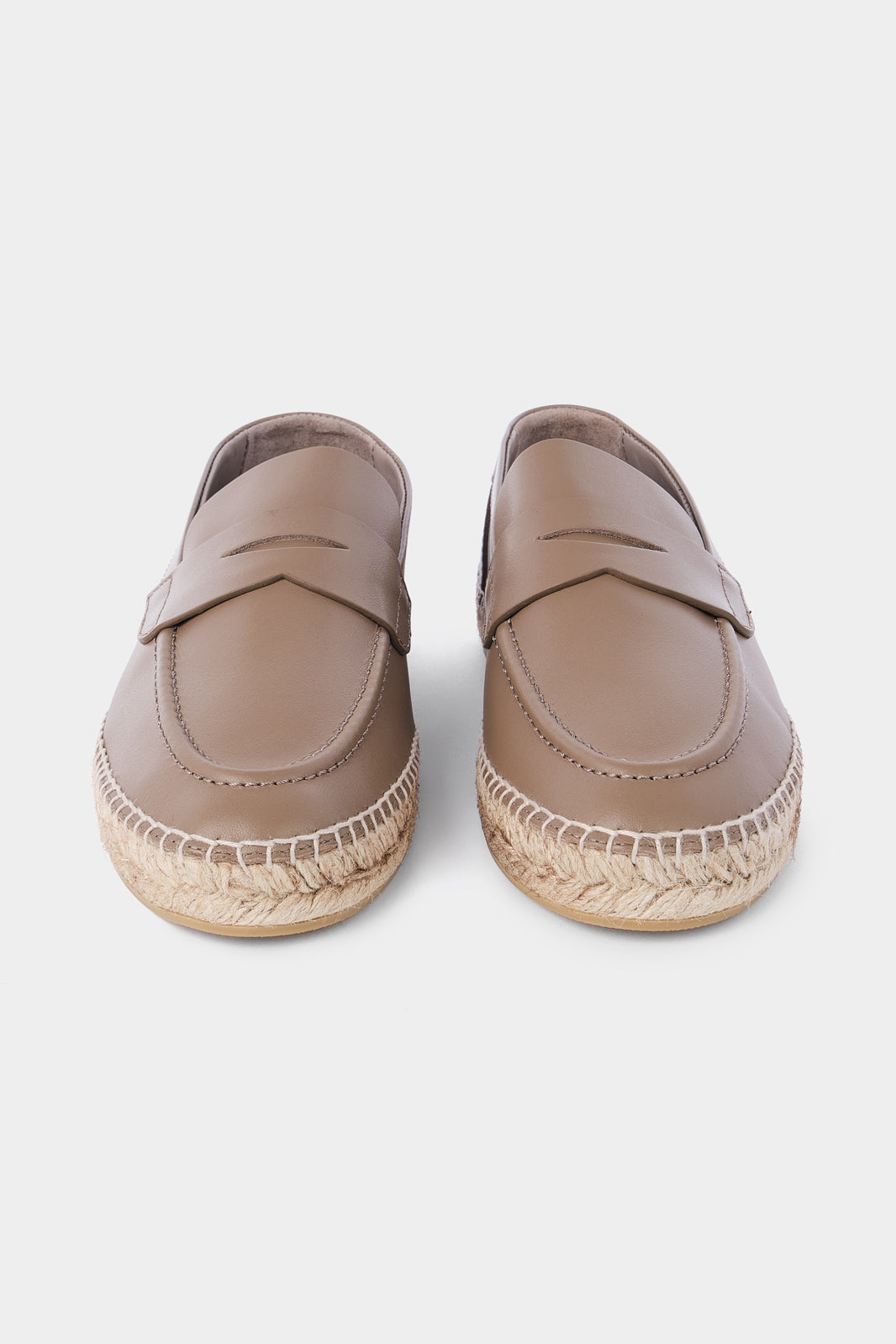 Une paire d'espadrilles en cuir beige avec des semelles en corde tressée. Les chaussures ont un design de mocassin avec des coutures apparentes sur le dessus.