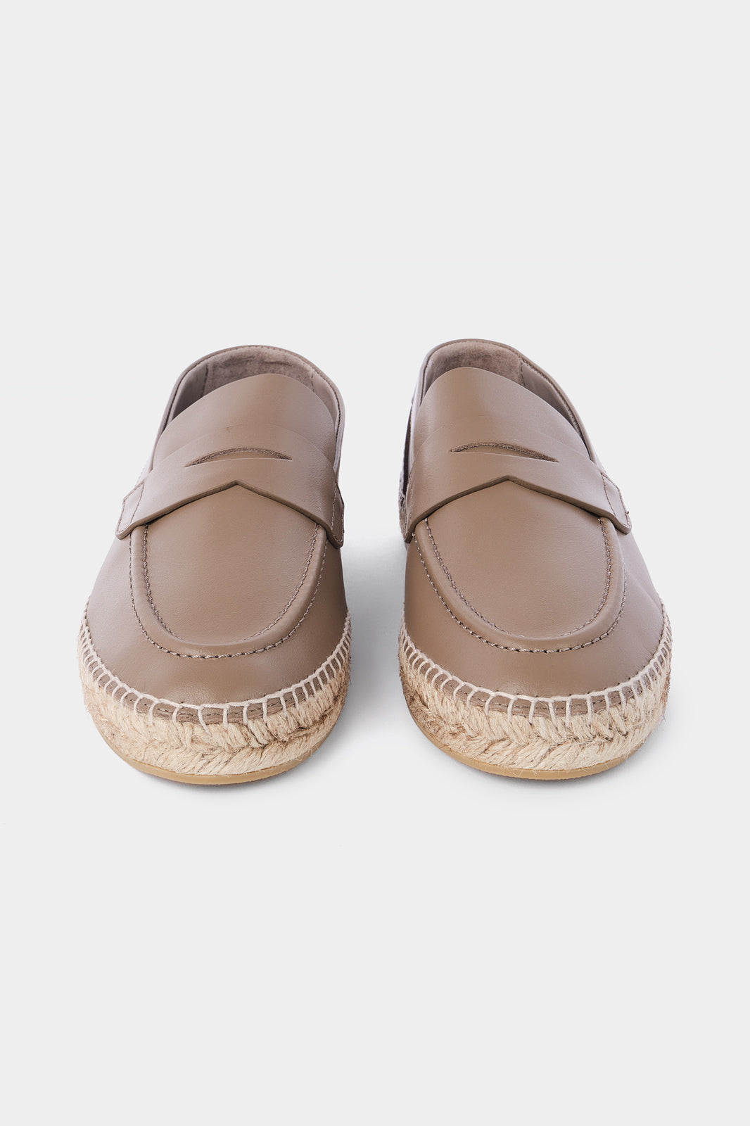 Une paire d'espadrilles en cuir beige avec des semelles en corde tressée. Les chaussures ont un design de mocassin avec des coutures apparentes sur le dessus.