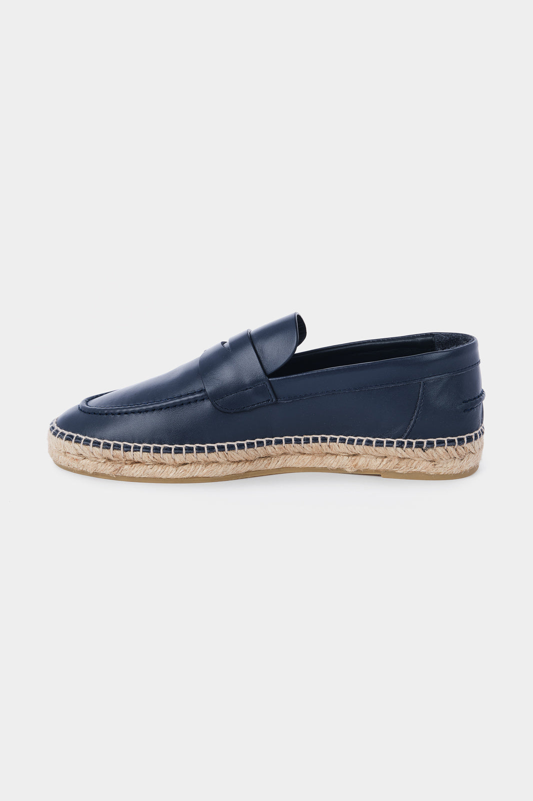 Vue de côté d'une espadrille en cuir bleu marine avec une semelle en corde tressée. Elle a un design de mocassin avec des coutures apparentes sur le dessus.