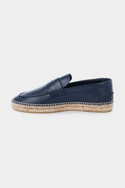 Vue de côté d'une espadrille en cuir bleu marine avec une semelle en corde tressée. Elle a un design de mocassin avec des coutures apparentes sur le dessus.