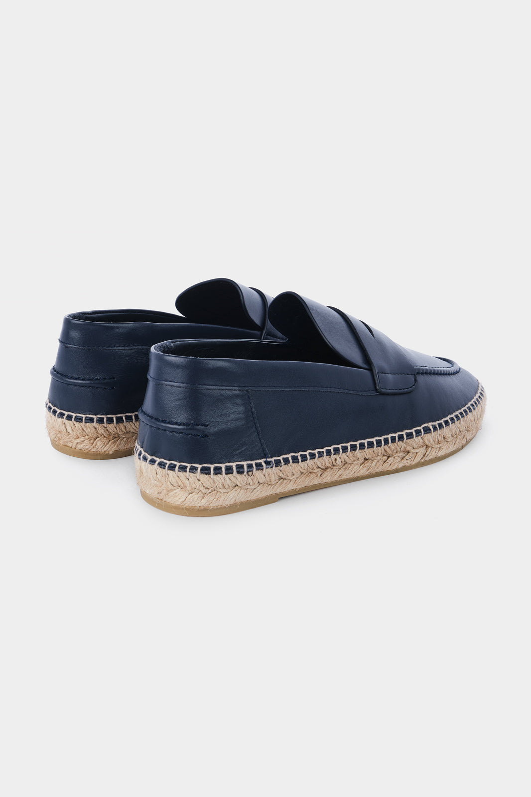 Vue de dos d'une paire d'espadrilles en cuir bleu marine avec des semelles en corde tressée. Les chaussures ont un design de mocassin avec des coutures apparentes sur le dessus.