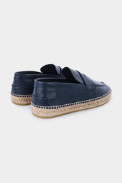Vue de dos d'une paire d'espadrilles en cuir bleu marine avec des semelles en corde tressée. Les chaussures ont un design de mocassin avec des coutures apparentes sur le dessus.
