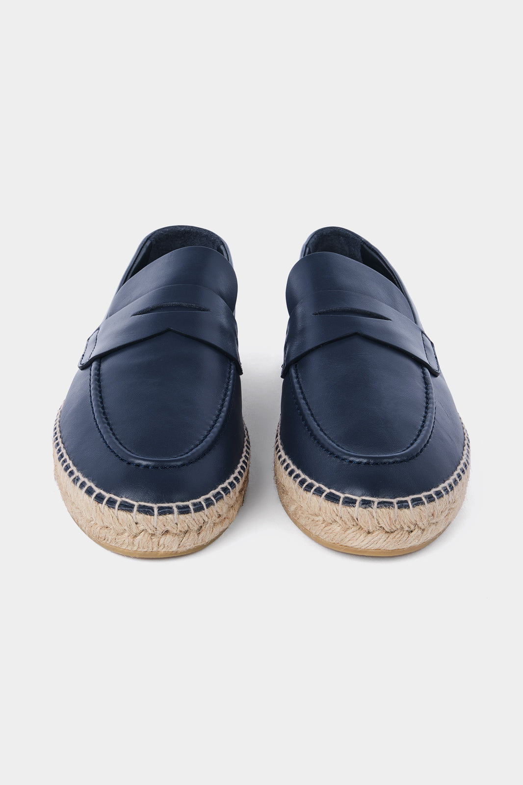 Une paire d'espadrilles en cuir bleu marine avec des semelles en corde tressée. Les chaussures ont un design de mocassin avec des coutures apparentes sur le dessus.