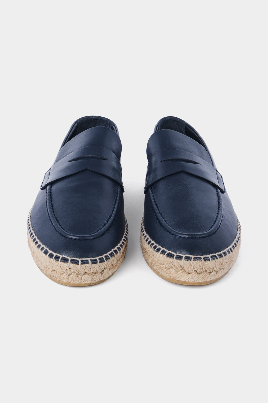 Une paire d'espadrilles en cuir bleu marine avec des semelles en corde tressée. Les chaussures ont un design de mocassin avec des coutures apparentes sur le dessus.