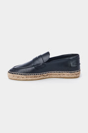 Vue de côté d'une espadrille en cuir noir avec une semelle en corde tressée. Elle a un design de mocassin avec des coutures apparentes sur le dessus.