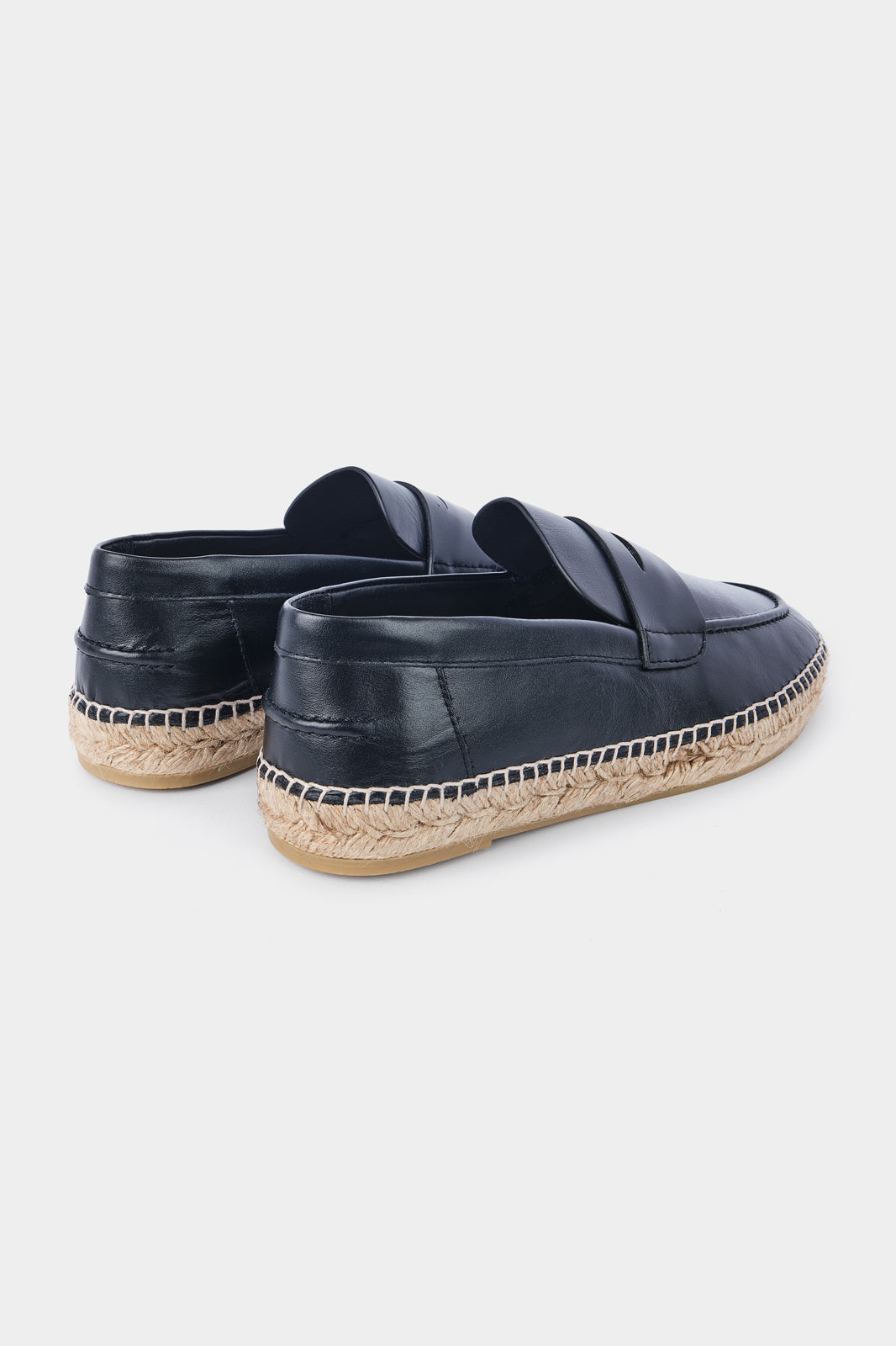 Vue de dos d'une paire d'espadrilles en cuir noir avec des semelles en corde tressée. Les chaussures ont un design de mocassin avec des coutures apparentes sur le dessus.