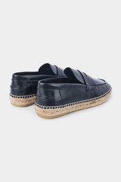 Vue de dos d'une paire d'espadrilles en cuir noir avec des semelles en corde tressée. Les chaussures ont un design de mocassin avec des coutures apparentes sur le dessus.