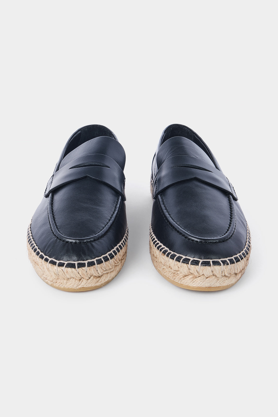 Une paire d'espadrilles en cuir noir avec des semelles en corde tressée. Les chaussures ont un design de mocassin avec des coutures apparentes sur le dessus.