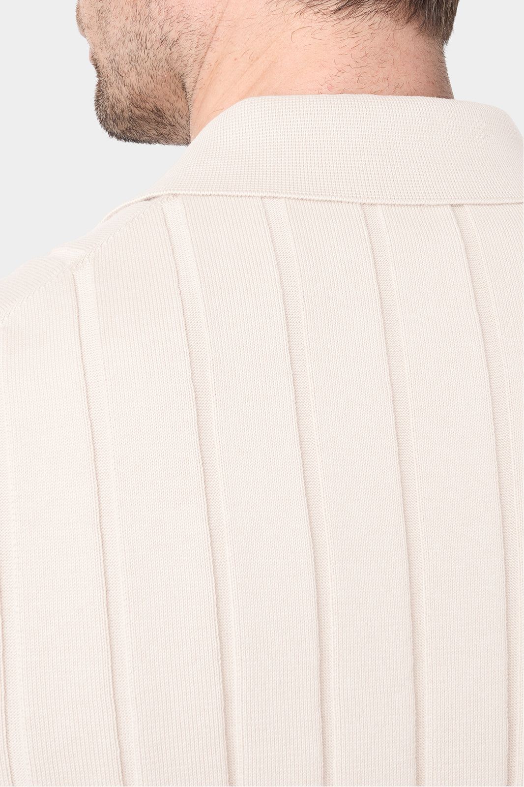 Un gros plan de dos d'une chemise polo beige avec des rayures verticales, mettant en évidence le col. Le tissu présente une matière en maille fine en coton.