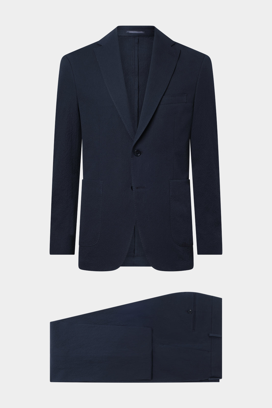 Vue sur fond blanc d'un costume seersucker marine ( aspect coton gauffré ) veste non doublée sans épaulette et poche napolitaine et d'un pantalon coupe traditionelle.