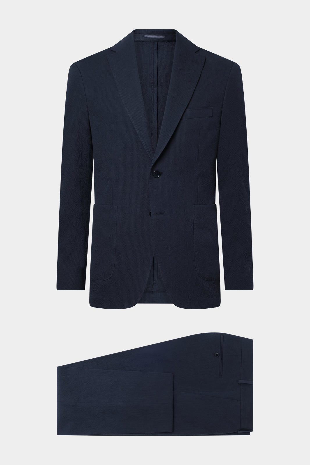 Vue sur fond blanc d'un costume seersucker marine ( aspect coton gauffré ) veste non doublée sans épaulette et poche napolitaine et d'un pantalon coupe traditionelle.