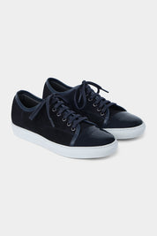 Vue sur fond blanc de la sneaker marine bout verni en peau et cuir vernir à lacet avec une semelle blanche épaisse.