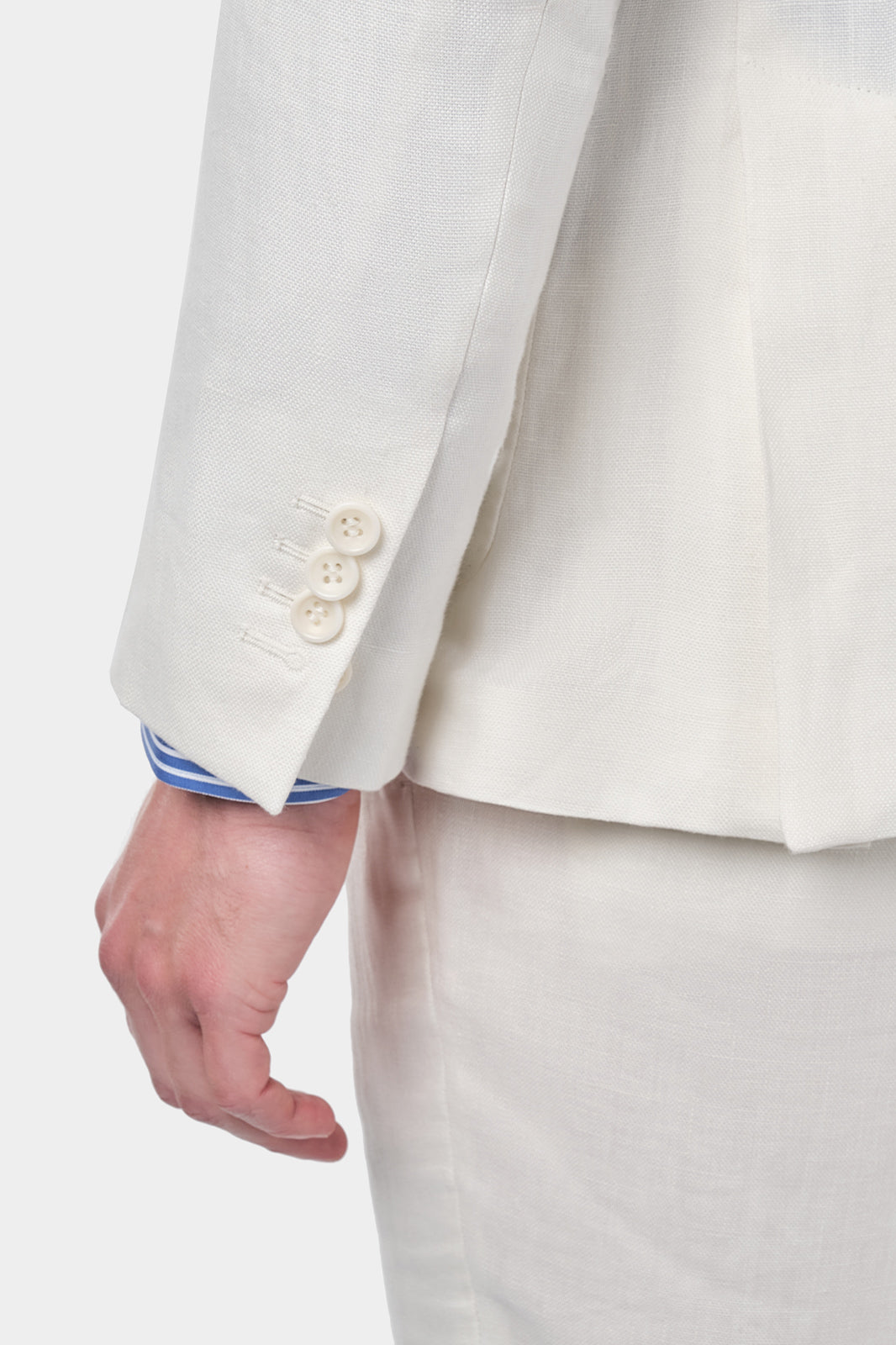 Zoom sur la manche du costume en lin blanc et de la chemise à rayure bleues et blanches que l’homme porte.