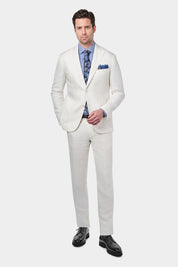 Homme portant un costume en lin blanc, avec une chemise à rayures bleues et blanches, une cravate à motifs bleus, et une pochette bleue dans la poche de la veste. Il poste également des souliers noirs.