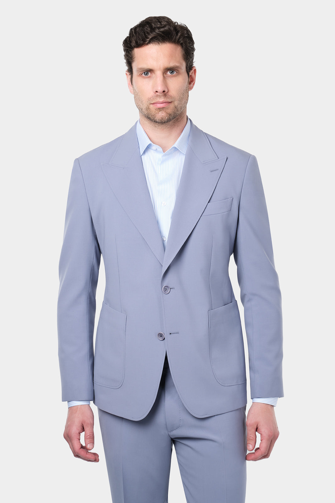 Homme portant un costume lilas à coupe cintrée, composé d'une veste à 2 boutons avec des poches plaquées et des revers en pointe, accompagné d'un pantalon assorti. Il poste également une chemise à rayures bleues et blanches.