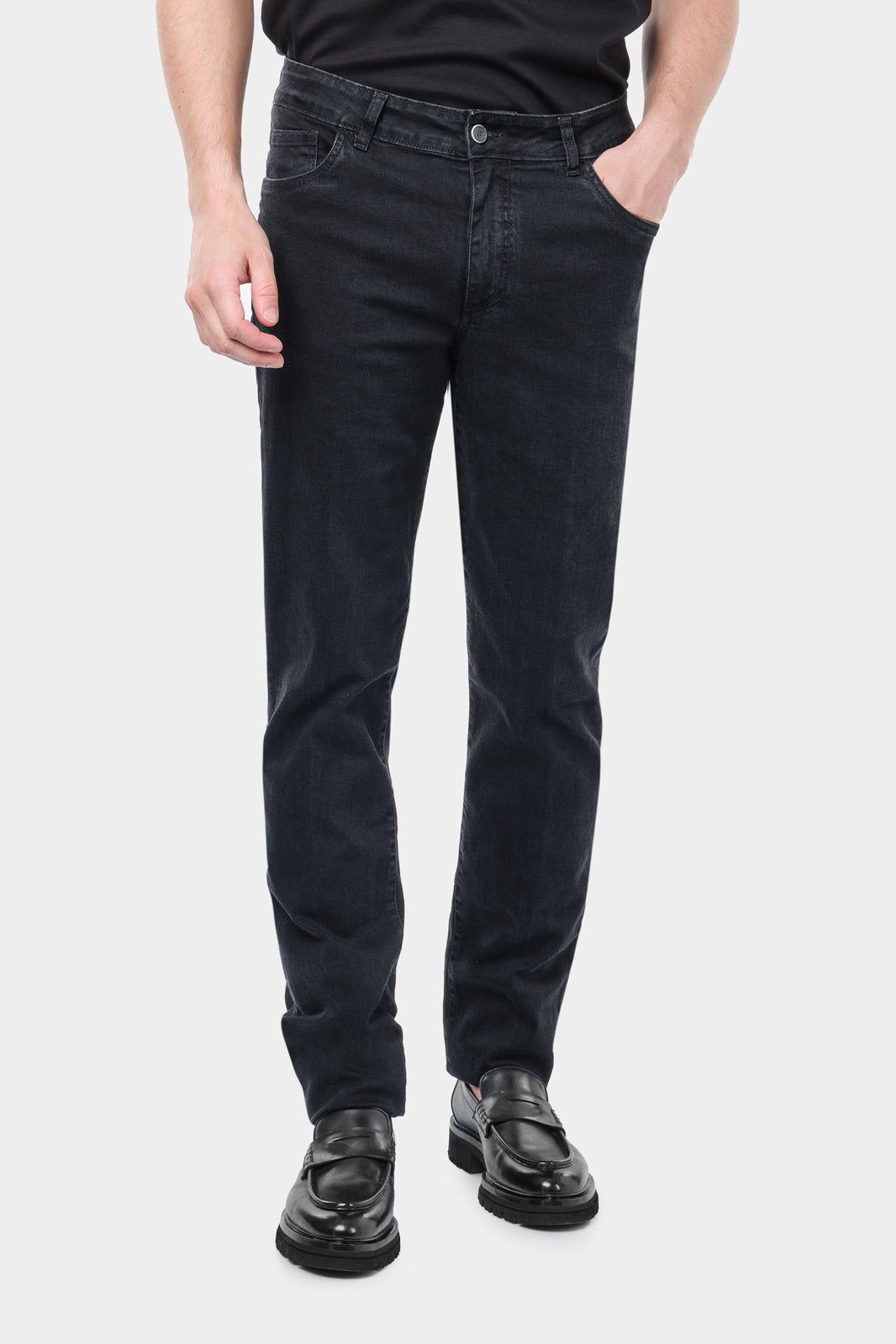 Un homme portant un jean en coton et élasthanne de couleur noire. Il porte également un tee-shirt en coton glacé noir et des mocassins en cuir noir.