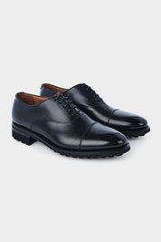 Vue sur fond blanc d'un soulier à lacets en cuir noir avec semelle épaisse et anti-dérapante.