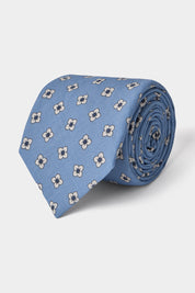 Vue sur fond blanc d'une cravate en tissu mélangé en bleu clair à motifs fleurs blanches et bleues