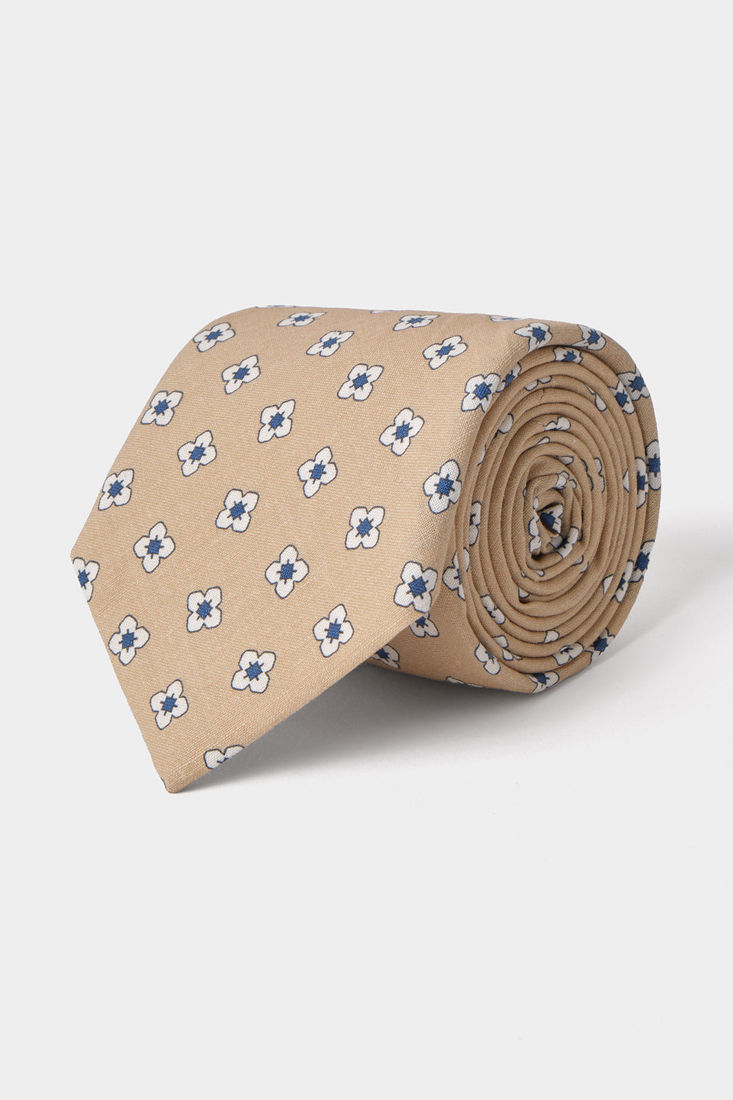 Vue sur fond blanc d'une cravate en tissu mélangé  couleur sable à motifs fleurs blanches et bleues 
