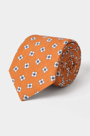 Vue sur fond blanc d'une cravate en tissu mélangé en orange à motifs fleurs blanches et bleues