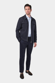 Un homme de dos vêtu d'un blouson bleu marine en tissu Olmetex imperméable et coupe-vent décontracté avec 4 poches, une fermeture à double zip et un col. Il porte également une chemise en coton à fines rayures bleues avec un col français et un pantalon bleu marine à pinces, accompagné de mocassins en daim marron.