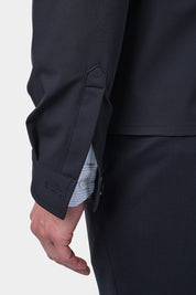 Un zoom sur la manche d'un homme vêtu d'un blouson bleu marine en tissu Olmetex imperméable et coupe-vent décontracté avec 4 poches, une fermeture à double zip et un col. Il porte également une chemise en coton à fines rayures bleues avec un col français et un pantalon bleu marine à pinces.