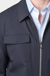  Zoom sur un homme vêtu d'un blouson bleu marine en tissu Olmetex, imperméable et coupe-vent, décontracté, avec quatre poches, une fermeture à double zip et un col. Il porte une chemise à rayures bleu ciel et blanches avec un col français.