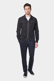 Un homme vêtu d'un blouson noir Danyberd en tissu Olmetex, imperméable et coupe-vent, décontracté, avec quatre poches, une fermeture à double zip et un col. Il porte un tee-shirt blanc en coton glacé et un pantalon bleu marine à pinces, accompagné de sneakers en bi matière veau velours.