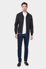 Un homme vêtu d'un blouson noir en tissu Olmetex, imperméable et coupe-vent, décontracté, avec quatre poches, une fermeture à double zip et un col. Il porte un tee-shirt blanc en coton glacé et un jean couleur brut accompagné de mocassins en daim marron.