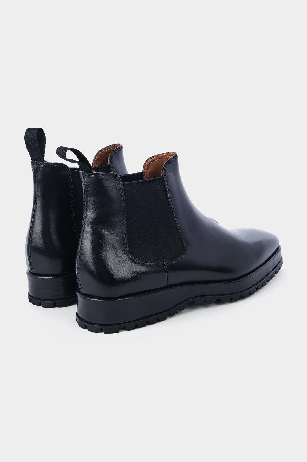 Paire de bottines Chelsea en cuir noir brillant avec des élastiques noirs sur les côtés et des languettes noires à l'arrière, posées sur un fond gris clair