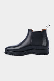 Paire de bottines Chelsea en cuir noir brillant avec des élastiques noirs sur les côtés et des languettes noires à l'arrière, posées sur un fond gris clair