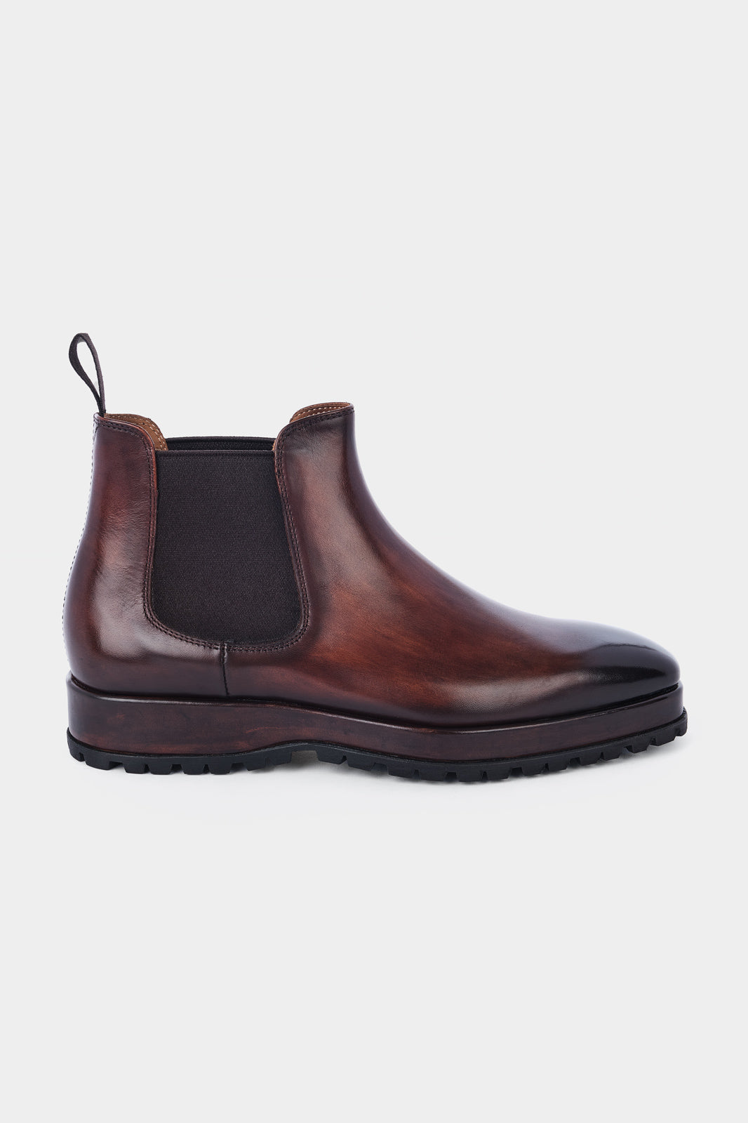 Paire de bottines Chelsea en cuir marron brillant avec des élastiques noirs sur les côtés et des languettes noires à l'arrière, posées sur un fond gris clair