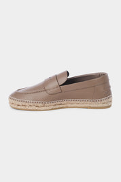 Vue de côté d'une espadrille en cuir beige avec une semelles en corde tressée. Elle a un design de mocassin avec des coutures apparentes sur le dessus. 