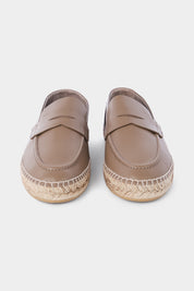 Une paire d'espadrilles en cuir beige avec des semelles en corde tressée. Les chaussures ont un design de mocassin avec des coutures apparentes sur le dessus.