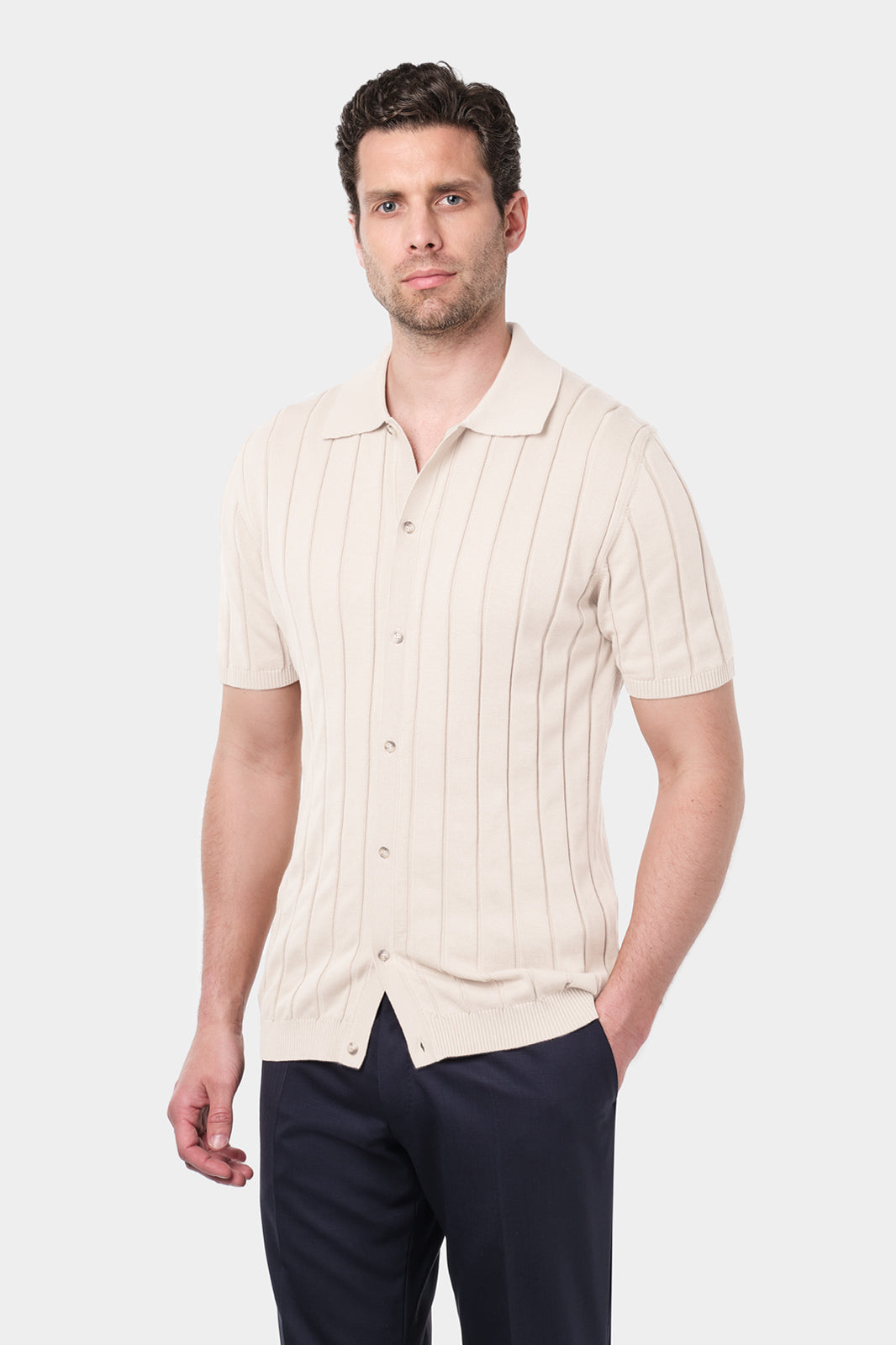 Un homme portant une chemise polo beige en coton avec des rayures verticales et un pantalon bleu marine. 