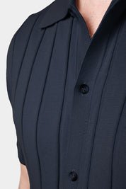 Un gros plan d'une chemise polo marine avec des rayures verticales, mettant en évidence les boutons et le col. Le tissu présente une matière en maille fine en coton.