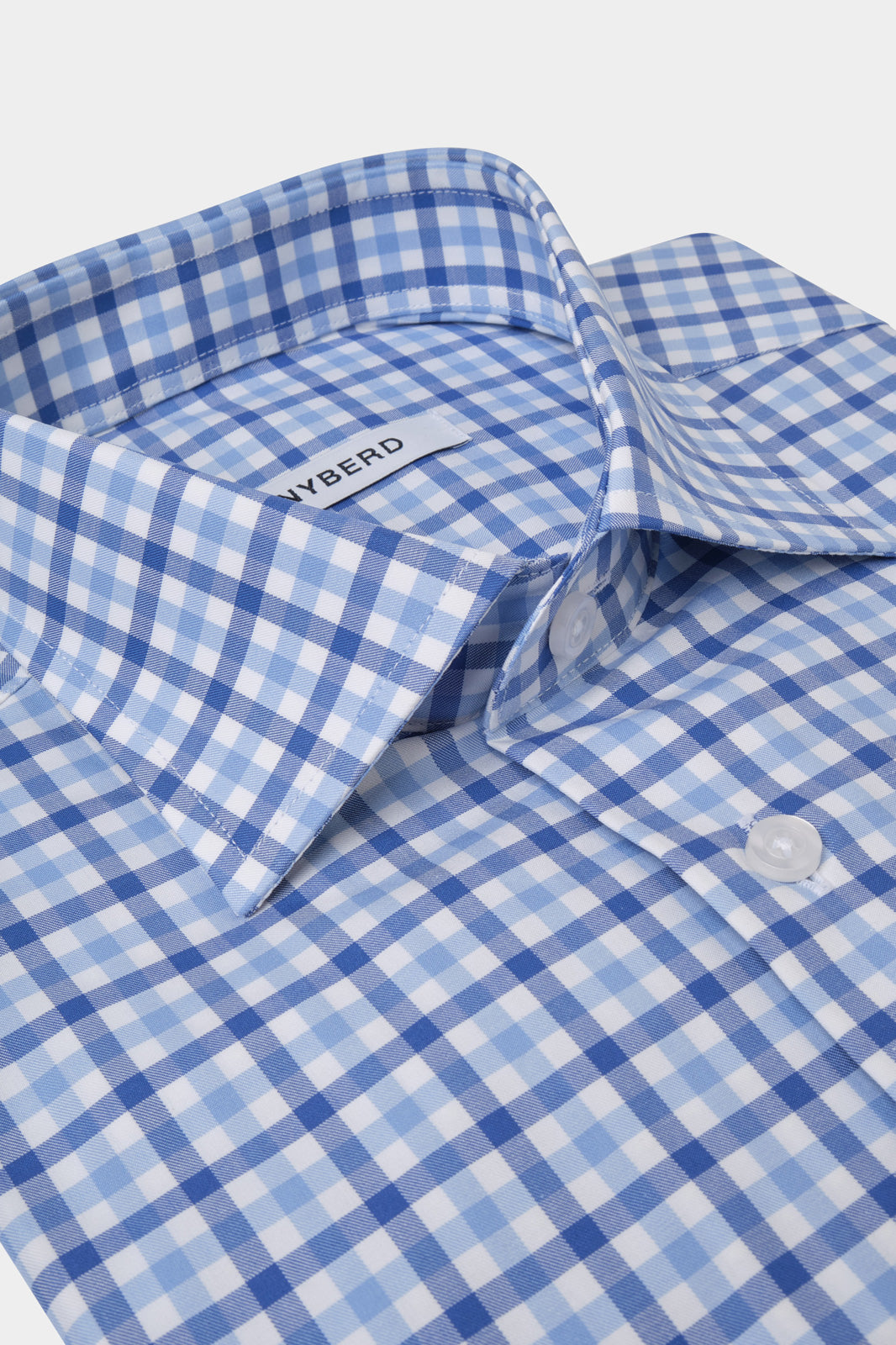 Vue sur fond blanc d'une chemise à carreaux bleu à col traditionnel et boutons apparents 