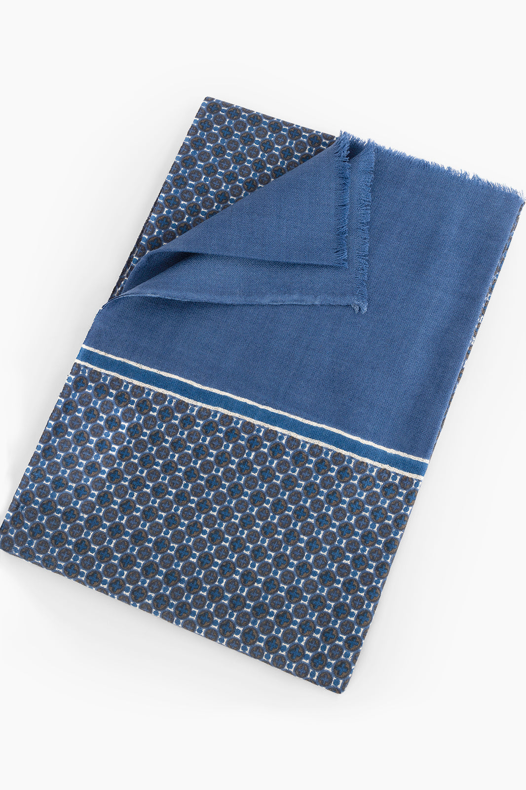 Chèche en laine bleu avec un motif géométrique circulaire en contraste, accompagné d'une bordure unie. L'écharpe présente des détails de franges fines aux extrémités, idéale pour un look moderne et élégant.