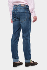  Homme de dos portant un jean en coton et élasthanne de couleur usé. Il porte également des mocassins en daim marron.  Il porte également une chemise en lin rose.