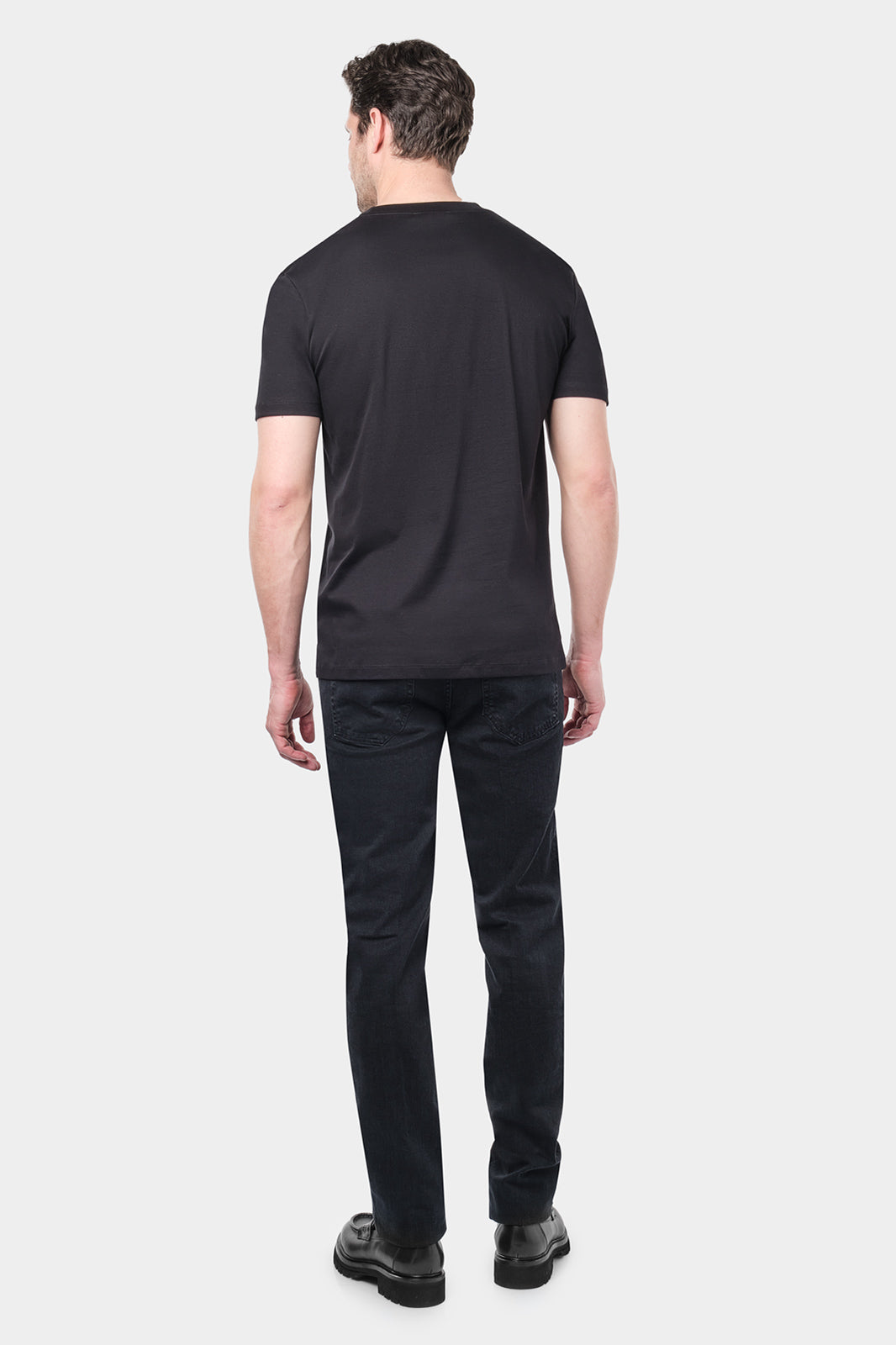 Homme de dos portant un t-shirt noir à manches courtes et un pantalon noir. Le t-shirt est simple et ajusté, et l'homme porte des chaussures noires.