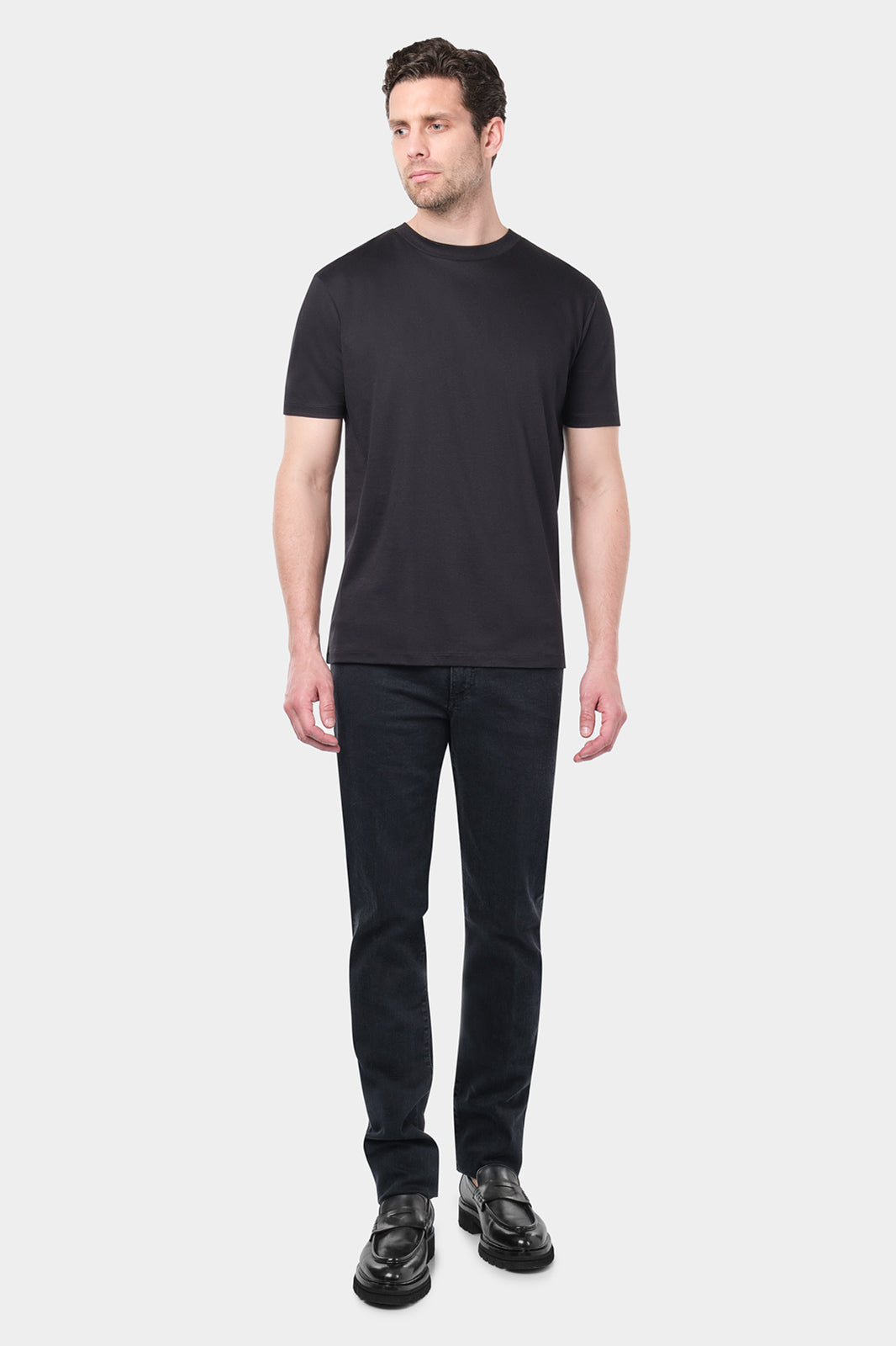 Homme de face portant un t-shirt noir à manches courtes et un pantalon noir. Le t-shirt est simple et ajusté, et l'homme porte des chaussures noires.